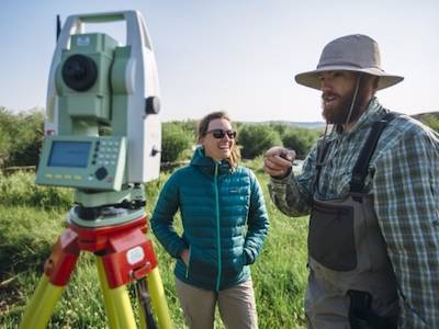 two MSU researchers in outdoors looking at surveying device