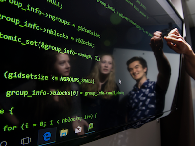 three students reflected on large computer screen displaying green code
