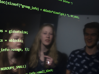 photo of large computer screen reflecting faces of three students